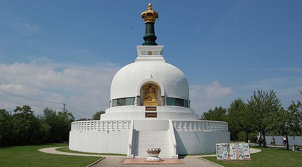 Eine weiße buddhistische Stupa von der Vorderseite, umringt von einem gepflegten Rasen an einem klaren, sonnigen Tag.