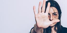 Frau mit blauem Auge hält Hand schützend vor sich in die Kamera