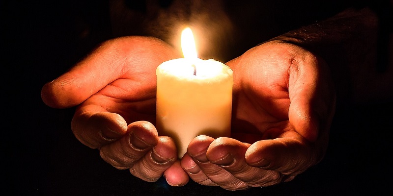 Das Bild zeigt zwei Hände, die eine Kerze halten.