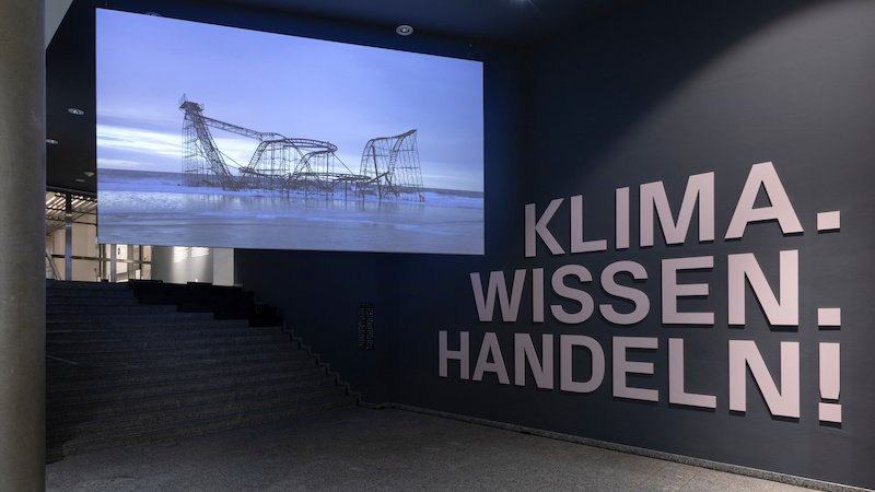 Filminstallation von Nikolaus Geyrhalter im Außenbereich der Dauerausstellung "Klima. Wissen. Handeln!" Auf der Wand steht in großen Lettern der Titel der Ausstellung.
