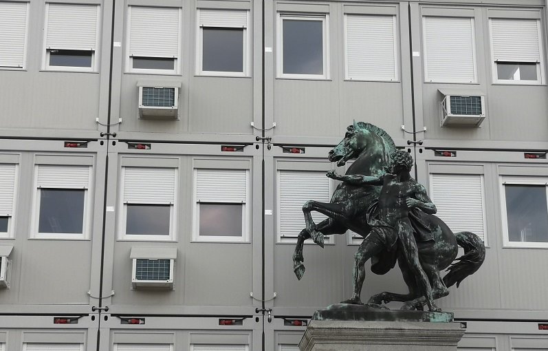 Das Bild zeigt eine Statue vor einer Containerwand.