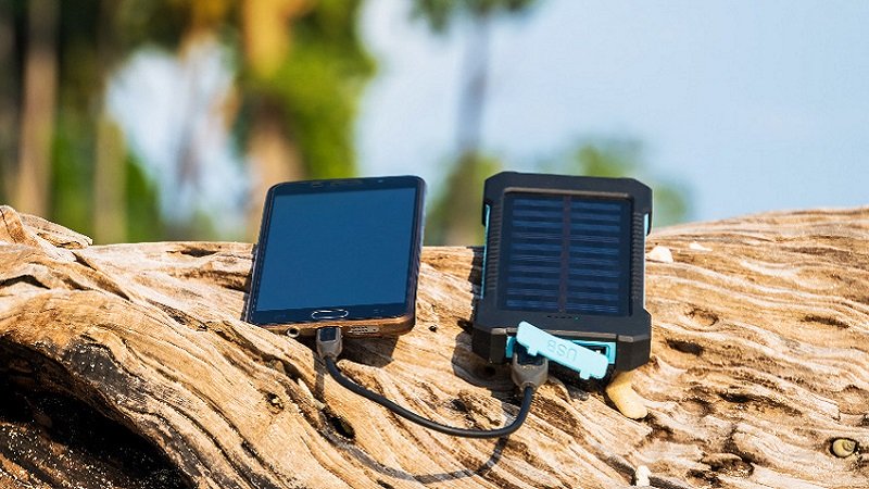 Solar Powerbank an der ein Handy angeschlossen ist liegt auf Baumstamm