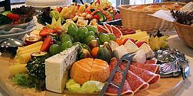 Große Platten mit Käse, Wurst, Obst und Gemüse. Dahinter Brot und Teller.