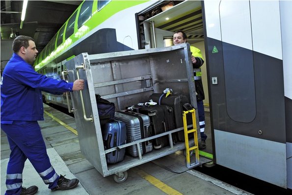 Gepäck wird von 2 Blaumännern in einem Metallcontainer in den CAT geschoben