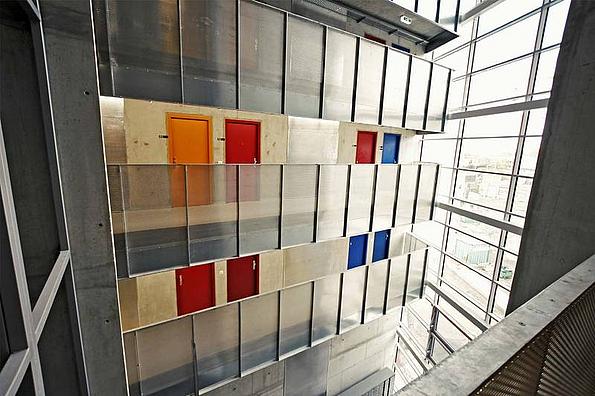 Innenansicht im Studentenwohnheim base 11. Blick im Stiegenhaus auf Stahl-Glas-Verkleidung mit integrierten roten, orangen und blauen quadratischen Elementen, die Glas-Stahl-Wand optisch auflockern.