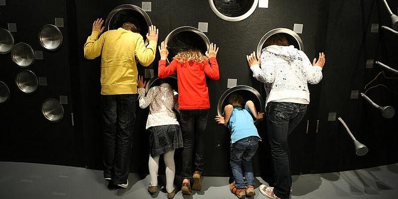 Fünf Kinder stecken ihre Köpfe in Löcher der Klanggalerie