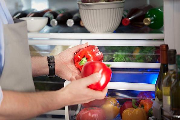 Mann hält zwei rote Paprika vor geöffnetem Kühlschrank
