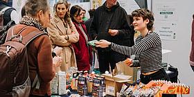 Besucher bei einem Messestand, Ausstellerin präsentiert Produkte