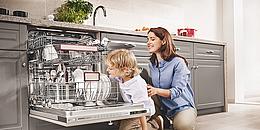 Mutter und Kind vor sauberem Geschirr im Geschirrspühler