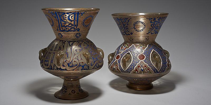 Zwei Gefäße mit Ähnlichkeit zu Vasen als Ausstellungsobjekte im Weltmuseum Wien. Diese beiden Moscheeampeln sind bunt verziert mit Emaildekor und haben eine Vergoldung.