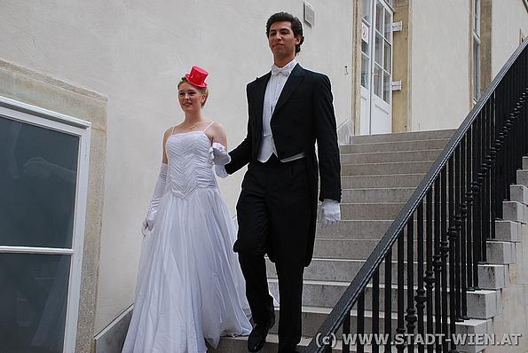 Elegant gekleidetes Paar, Dame in schneeweißem Kleid, Herr im Frack, steigt eine Treppe hinunter
