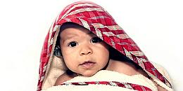 Ein Baby aug weißen Handtüchern mit einer Decke über dem Kopf