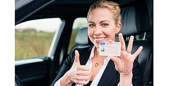 Frau sitzt im Auto lächelt und hält den Führerschein hoch