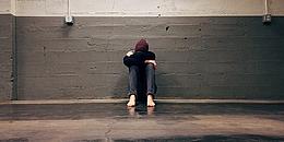 Angststörungen: Mann sitzt zusammengekauert an einer Wand und fürchtet sich