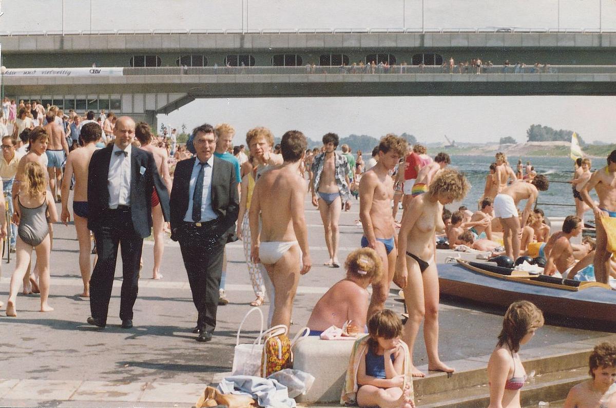 Helmut Zilk spaziert im Anzug mit einem anderen Mann vorbei an badenden Leuten auf der Donauinsel