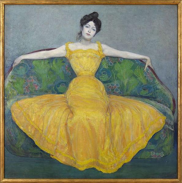 Junge Frau mit bleicher Haut und langem gelben Kleid sitzt mit ausgebreiteten Armen auf einem grünen Sofa