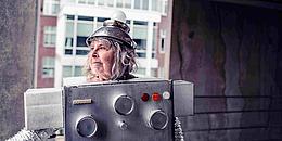 Zu sehen ist eine ältere Frau in einem Roboter-Kostüm.