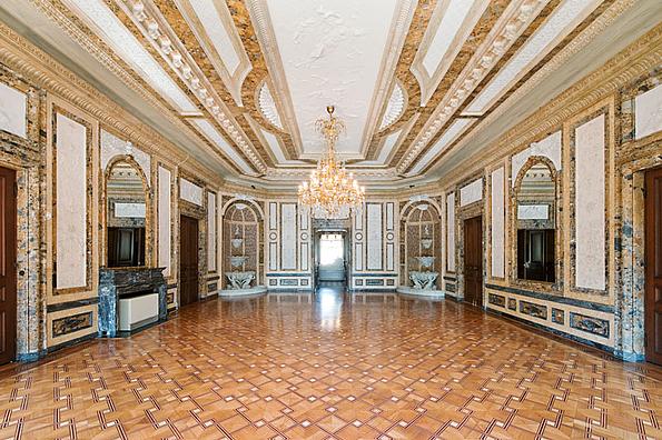 Ein Prunksaal in Rosétönen gehalten mit vielen Spiegeln und einem Kronleuchter.