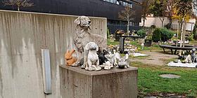 Auf einer hüfthohen Betonsäule sind Statuen von Haustieren wie Hunde und Katzen zu sehen. Im Hintergrund sind kreisförmig nebeneinander angelegte Tiergräber zu sehen.