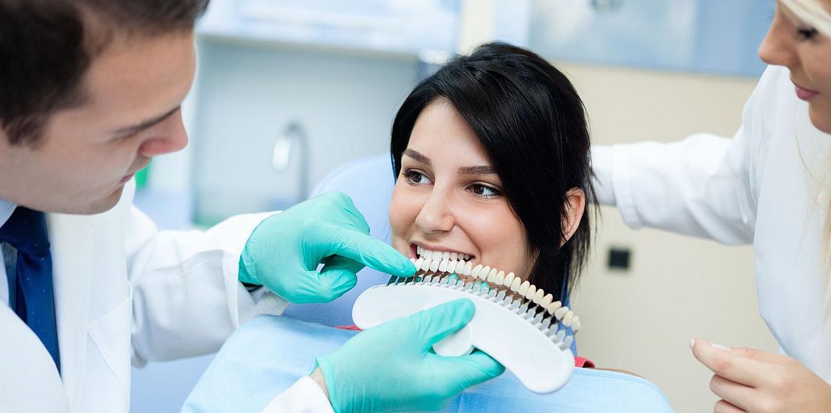 Zahnarzt zeigt Farbkarte zu den Zähnen einer Patientin