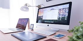 Mehrere Apple Geräte (Mac Pc, Macbook, iPhone, iPad) auf einem Schreibtisch.