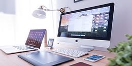 Mehrere Apple Geräte (Mac Pc, Macbook, iPhone, iPad) auf einem Schreibtisch.