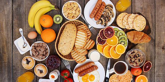 Obst, Brot, Wurst, Kaffee und Säfte auf einem Holztisch verteilt.