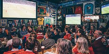 Menschen die gemeinsam in einer Bar auf einem Fernseher Sport schauen.
