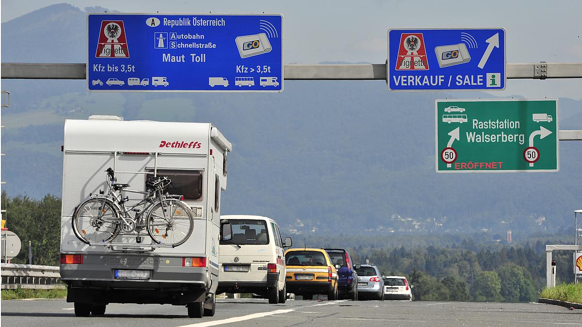 Bild von Autos auf österreichischer Autobahn. Autobahnschild weist auf Vignetten-Verkaufsstelle hin.