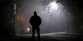 Silhuette eines Mannes in der Nacht, er wird von einer Straßenlaterne sichtbar gemacht