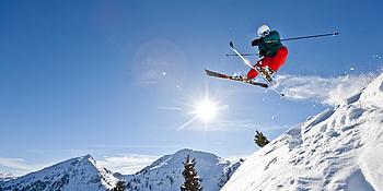 Skifahrer springt, Schnee staubt, Sonne scheint am blitzblauen Himmel