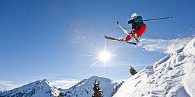 Skifahrer springt, Schnee staubt, Sonne scheint am blitzblauen Himmel