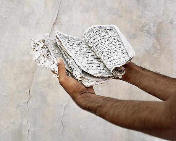 Zwei Hände, bis zu den Ellbogen fotografiert, halten zerfledertes Buch mit arabischem Text
