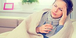 Frau liegt auf Couch mit Glas Wasser in der Hand und ist krank wegen Biowetter