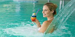 Frau sitzt mit Cocktail in Pool und lächelt