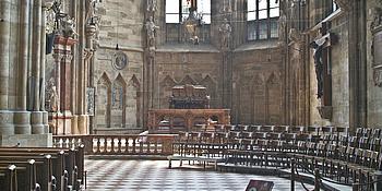 Stephansdom von innen, mit Blick auf das Grab von Friedrich III.: links stehen Kirchenbänke, rechts hängt ein Kreuz.