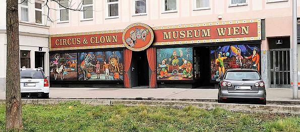 Die Vorderseite eines Clownmuseum, wobei der Eingang mit roten Vorhängen verziert ist und auf der Fassade Zirkusmalereien zu sehen sind.