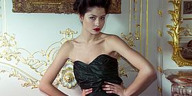 Model in schwarzem Kleid vor barocker Wand