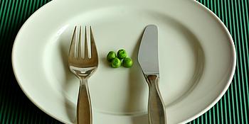 Erbsen und Gabel und Messer auf einem weißen Teller vor grünem Hintergrund