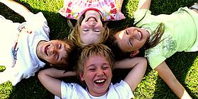 Vier Kinder, die mit ihren Köpfen an- und nebeneinander einen Kreis im Gras bilden 