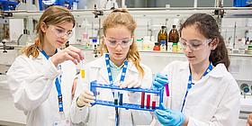Das Bild zeigt drei Mädchen mit naturwissenschaftlicher Ausrüstung. 