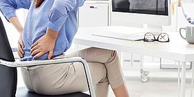 Rückenschmerzen: Frau sitzt am Laptop und hält sich unteren Rücken