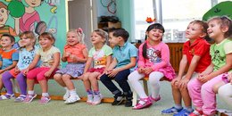 Kleine Kinder, die im bilingualen Kindergarten auf einer Bank sitzen