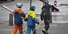Drei Skifahrer in der Stadt, mit Skiern über den Schultern.