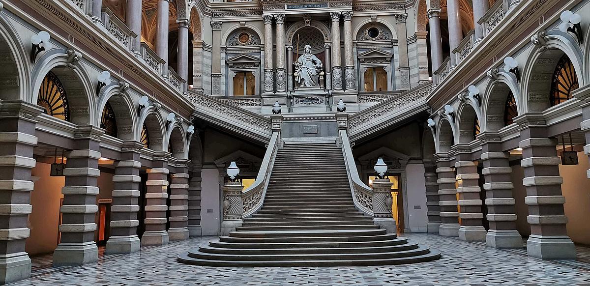 Eine imposante Halle aus Marmor mit einer Treppe in der Mitte, die zu einer Statue der Gerechtigkeitsgöttin Justitia führt