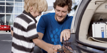 Kind und Mann stecken Stromkabel ins Elektroauto. 