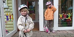 Das Bild zeigt zwei Kinder vor dem Eingang eines Kindergartens. 