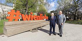 Michael Ludwig und Walter Ruck vor einem Schild mit dem Schriftzug "#wienliebe" im Wiener Rathauspark.