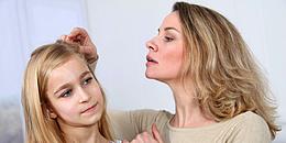 Blonde Mutter, die den Kopf und die Haare ihrer blonden Tochter auf Läuse untersucht