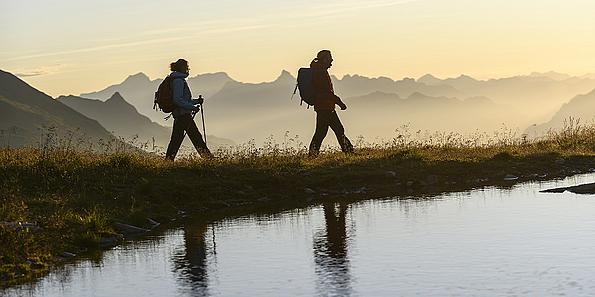Pärchen wandert im Sonnenaufgang an See in Bergen vorbei